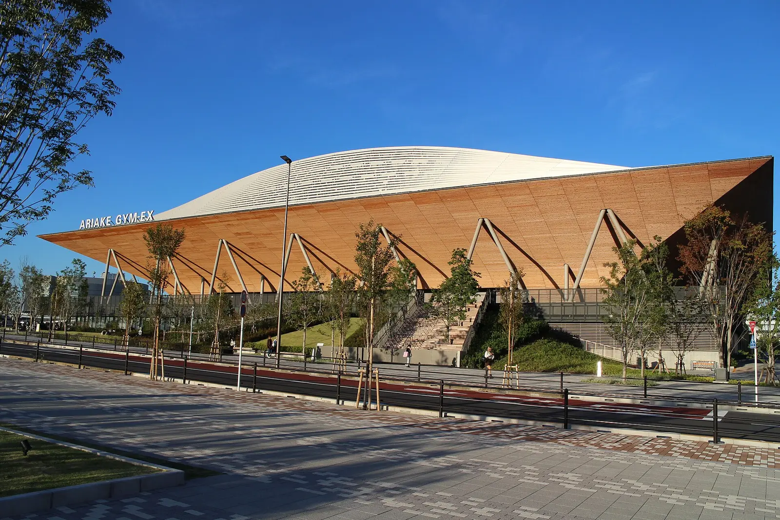 Wooden roofed Ariake GYM-EX exhibition hall in Tokyo with its name on the facade under a deep blue sky