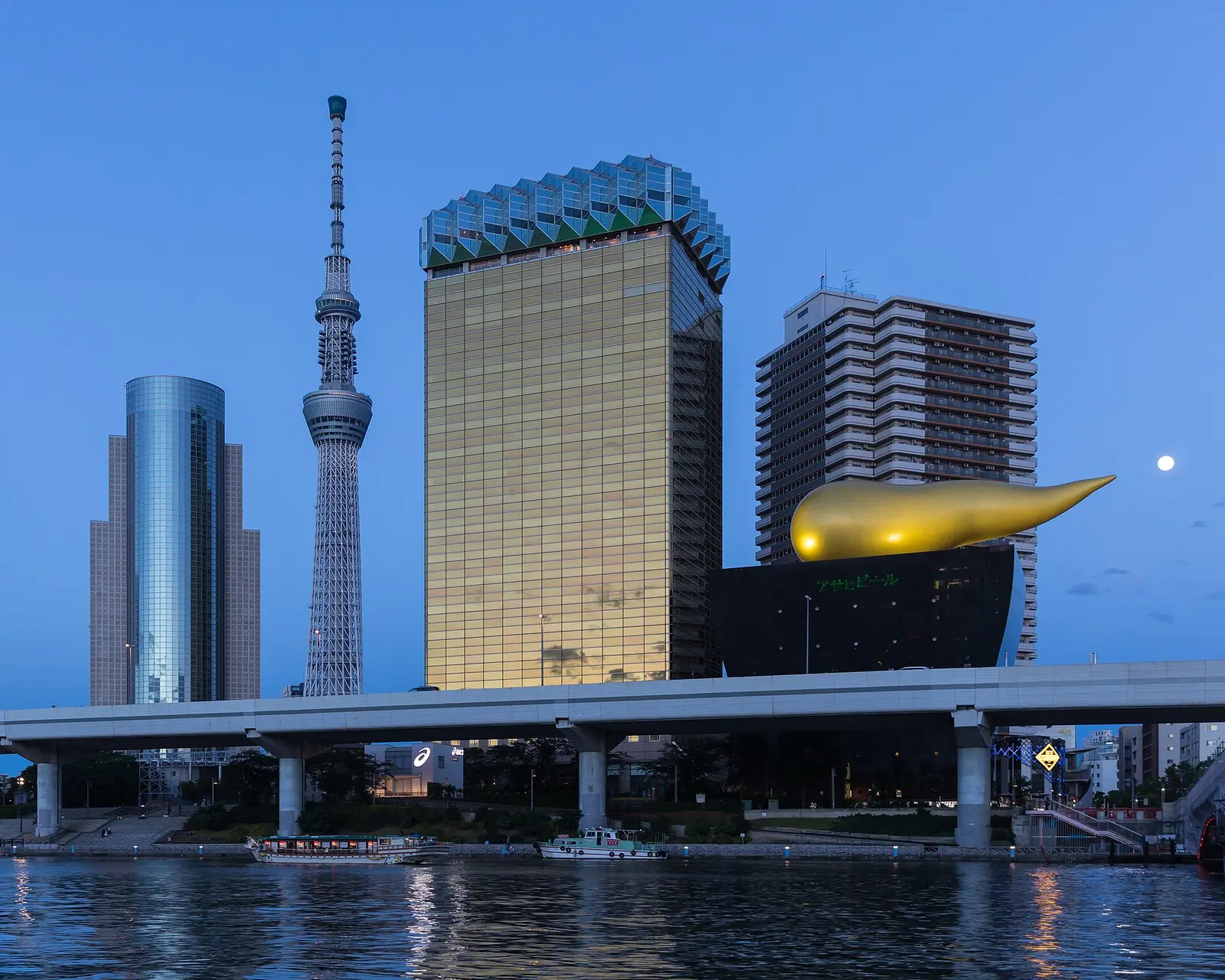 Tokyo Skytree rising behind the Asahi headquarters buildings beside the Sumida River at blue hour