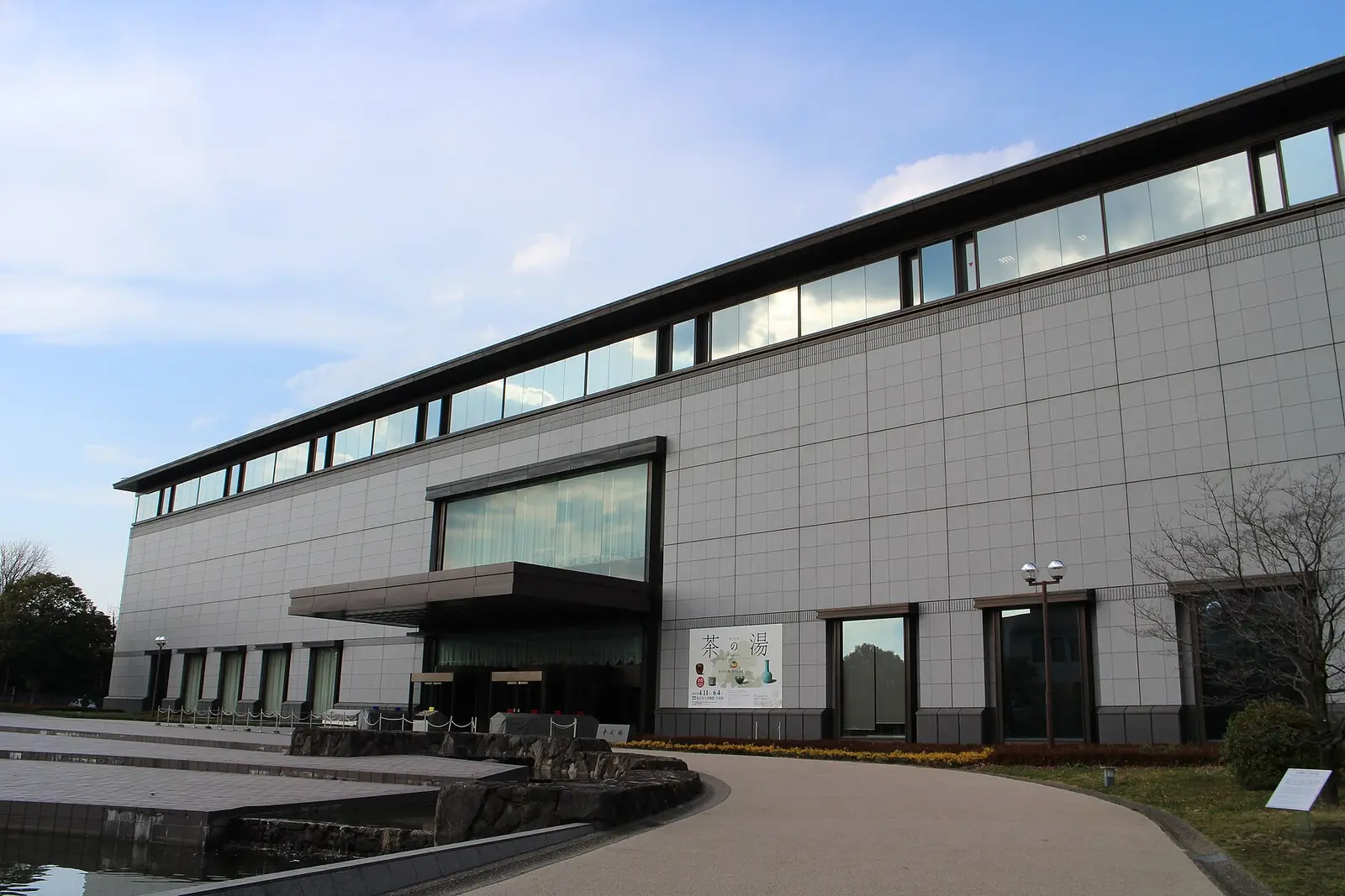 Long grey glass fronted Heiseikan building of the Tokyo National Museum beside a pond in Ueno Park